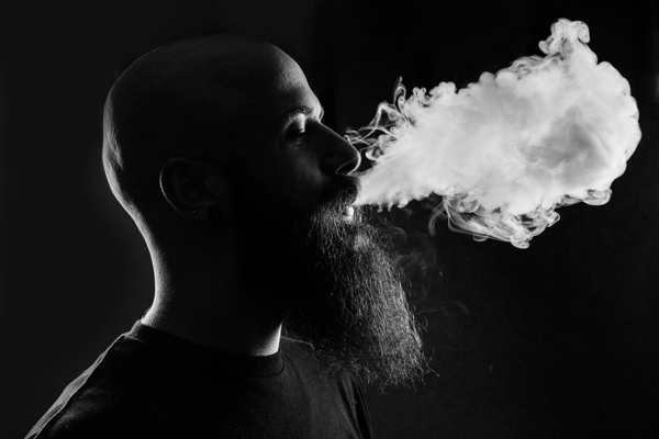a bald man blowing big clouds from vaping in a black and white contrast