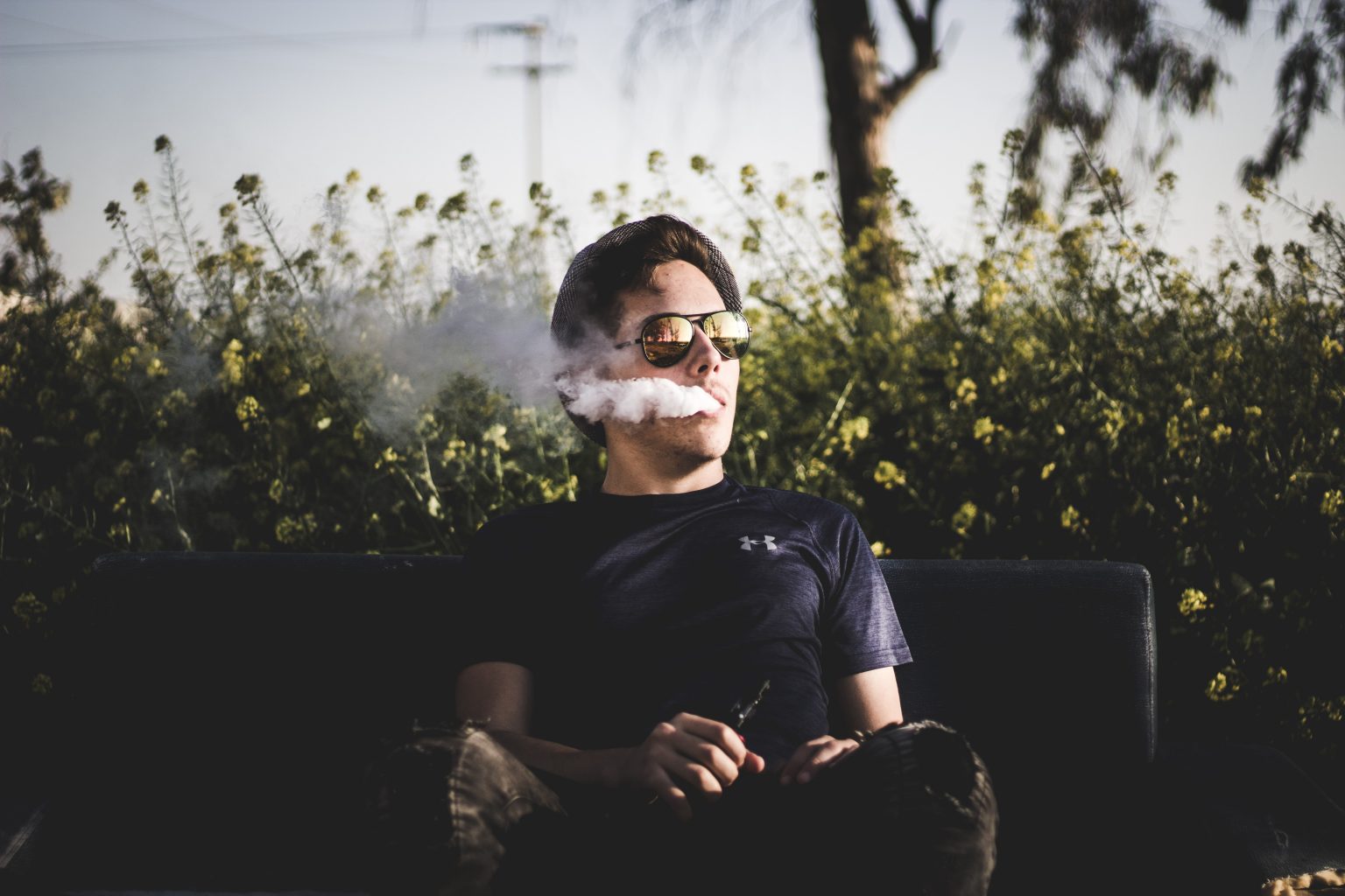 a man wearing a black under armour tshirt vaping on a bench in a park