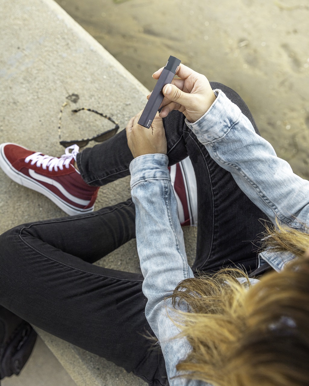 a woman in double denim and red vans holding a vaping device