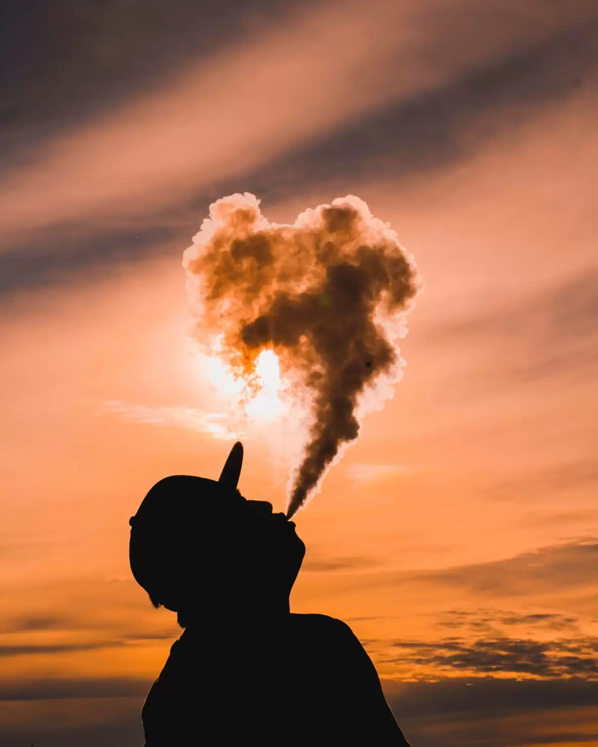 A person wearing a cap blows a vape into the air