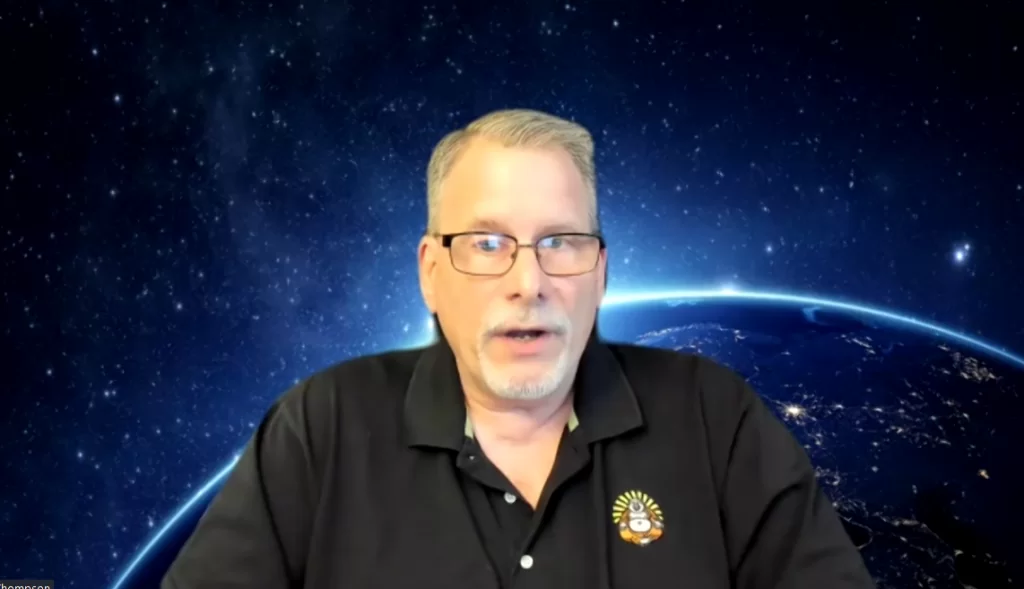 A man sits in front of a blue earth screen on Zoom