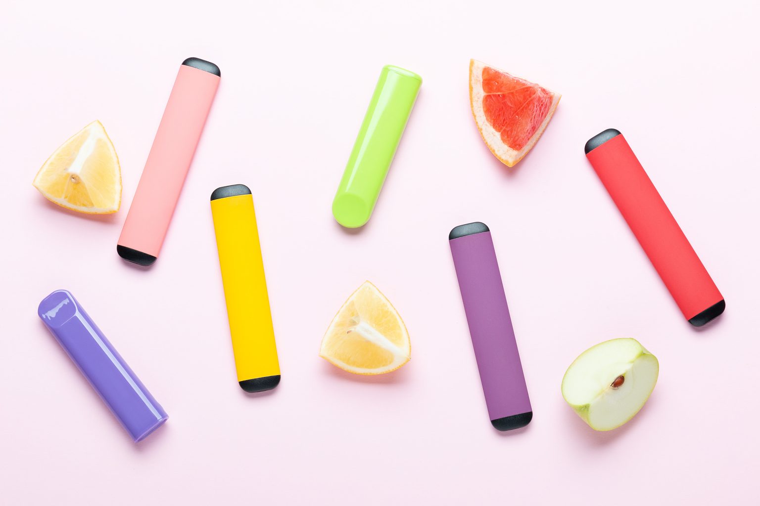 multi-coloured e-cigarettes with different fruit placed on a pink background